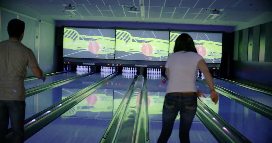 Man and woman roll their bowling balls down the lanes
