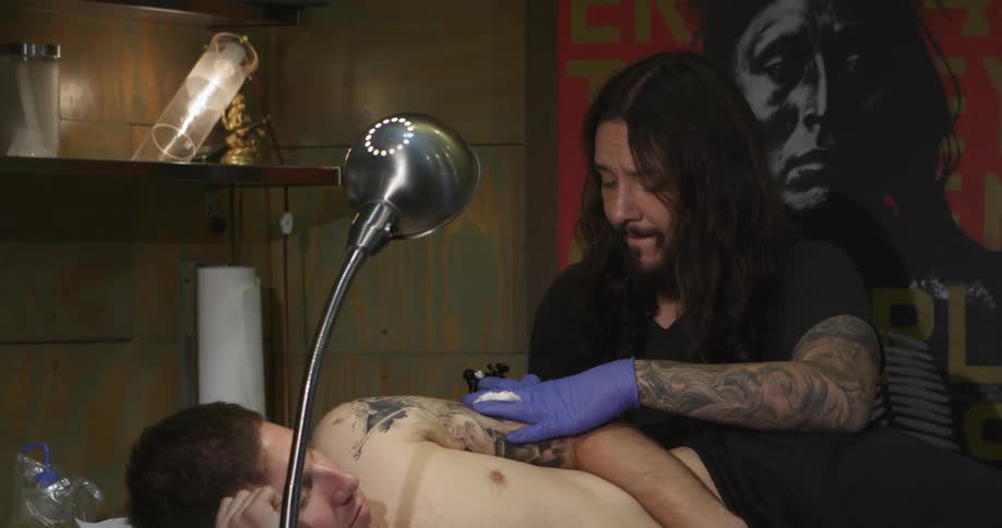 Male tattoo artists working on the arm of a male customer