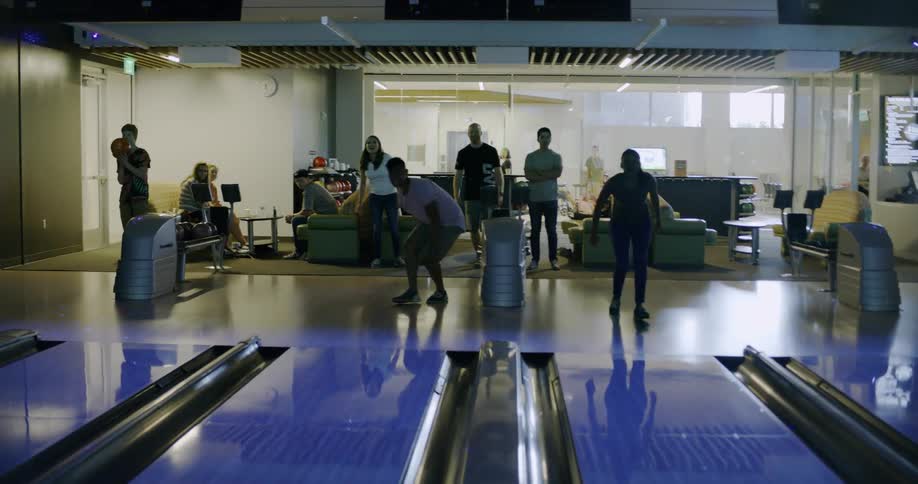Friends roll bowling balls down a lane