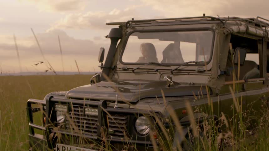 A woman leans out of a truck parked in the grasslands