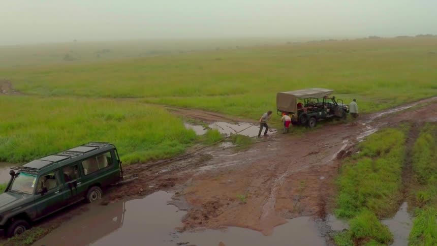 A jeep is being pulled from the mud by another jeep and some people