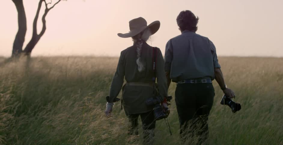 A man and woman carrying cameras walk through a field