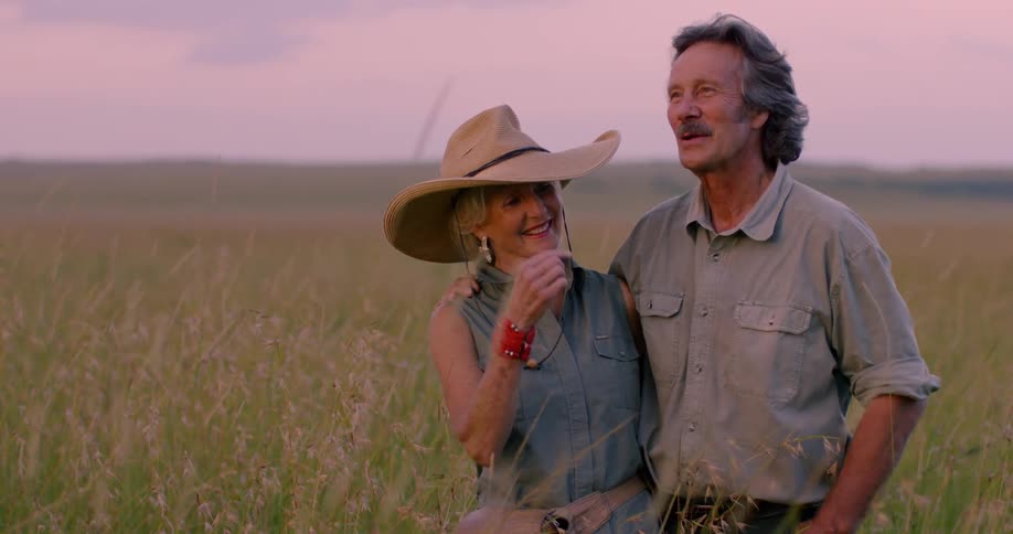 Man and woman stand in grassy field at sunset