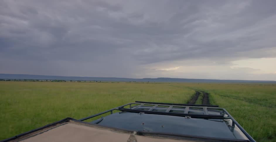 A jeep is riding along a dirt road with a storm in the distance behind them