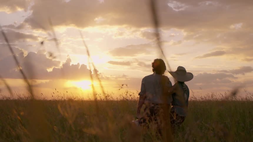 A man is carrying a camera as he stands with a woman looking at the sunset