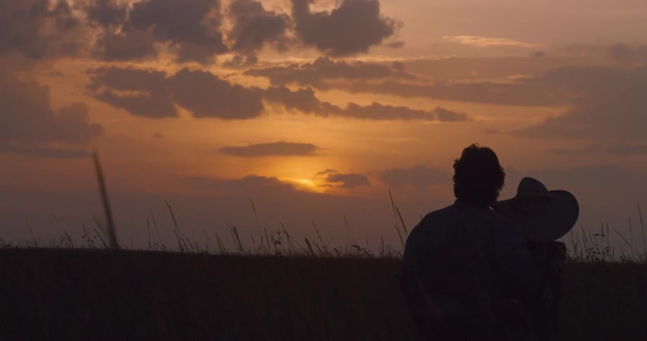 A couple sit in the grass watching the sun set