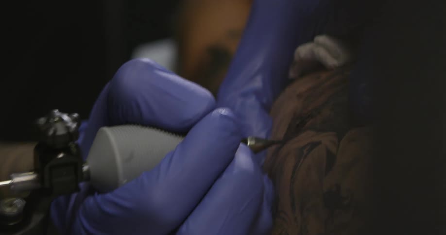 A blue-gloved tattoo artist filling in a tattoo
