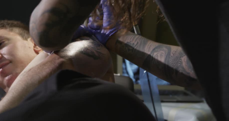 A tattoo artist works on a client