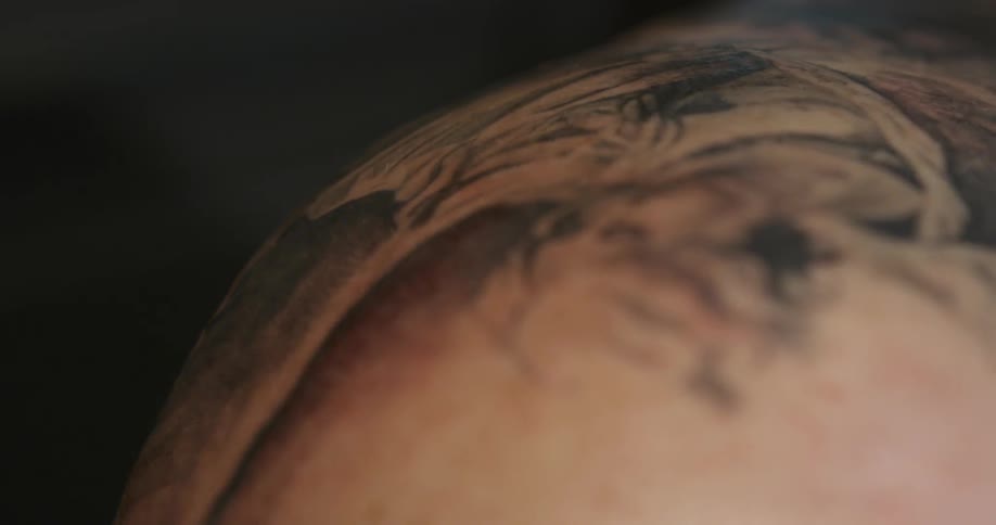 A person wipes down a fresh tattoo on a persons body