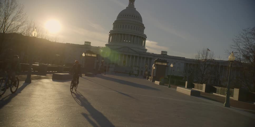 Bicyclists ride in front of a capitol building at sunset
