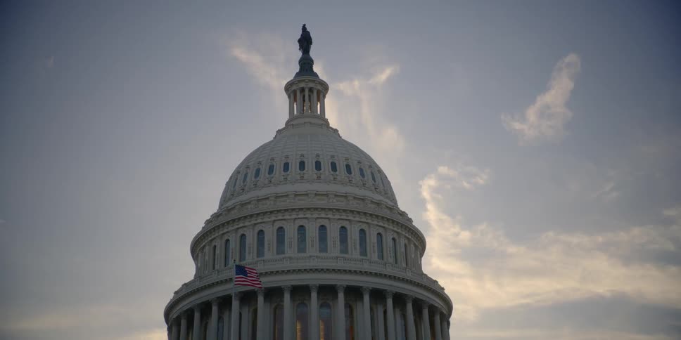 An american flag billows in front of a capitol building