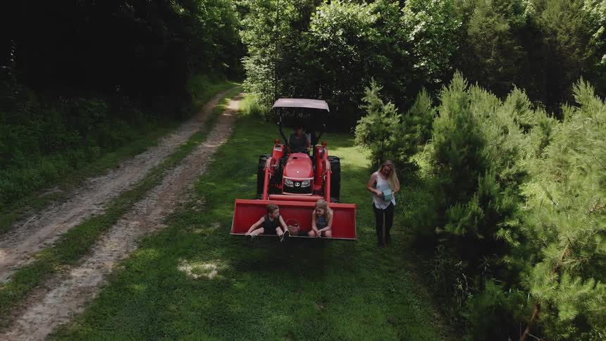 A woman is walking alongside a plow carrying children