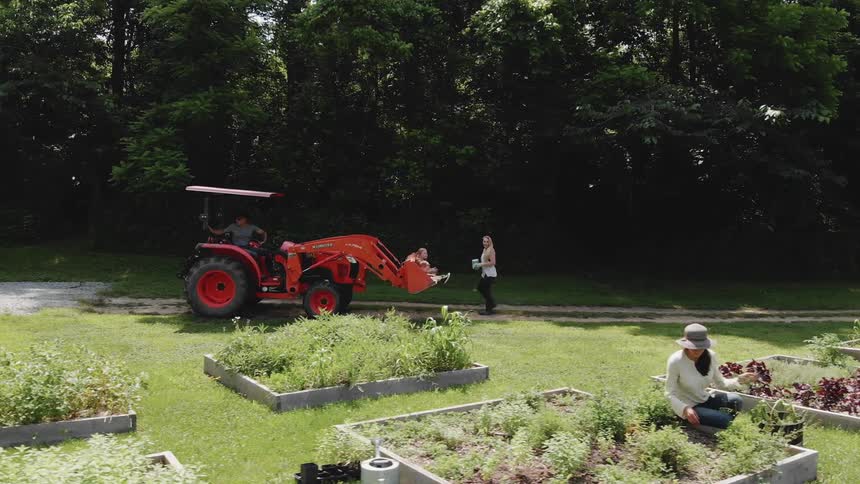 A tractor is backing down a dirt road next to a garden