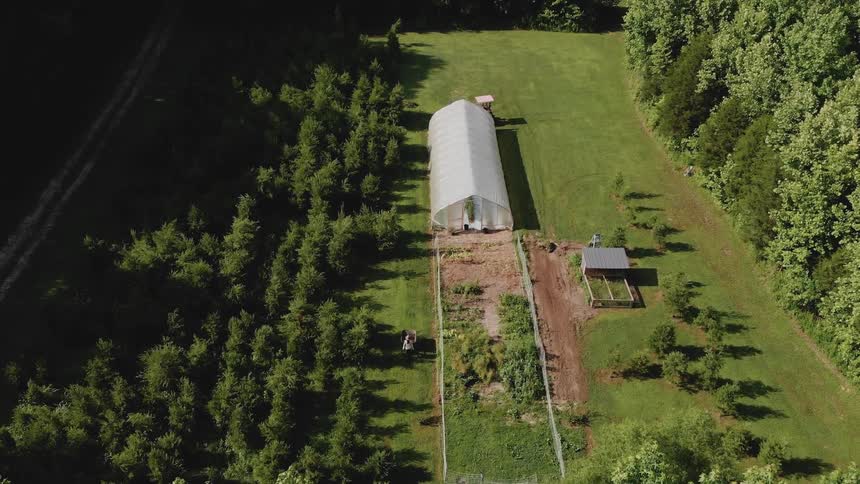A tractor drives behind a farm greenhouse