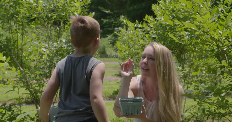 A woman tosses a berry at a boy waiting with open mouth