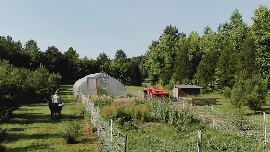 A tractor and a person with a wheelbarrow are working on a small garden