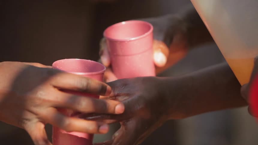 People getting cups filled with liquid from a pitcher