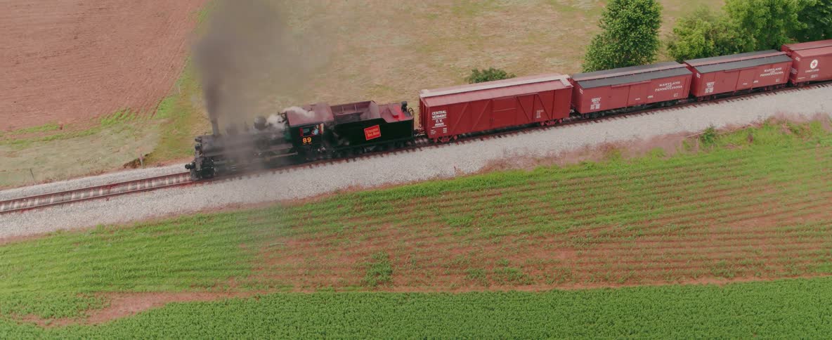 A black train is pulling many red trailers of cargo