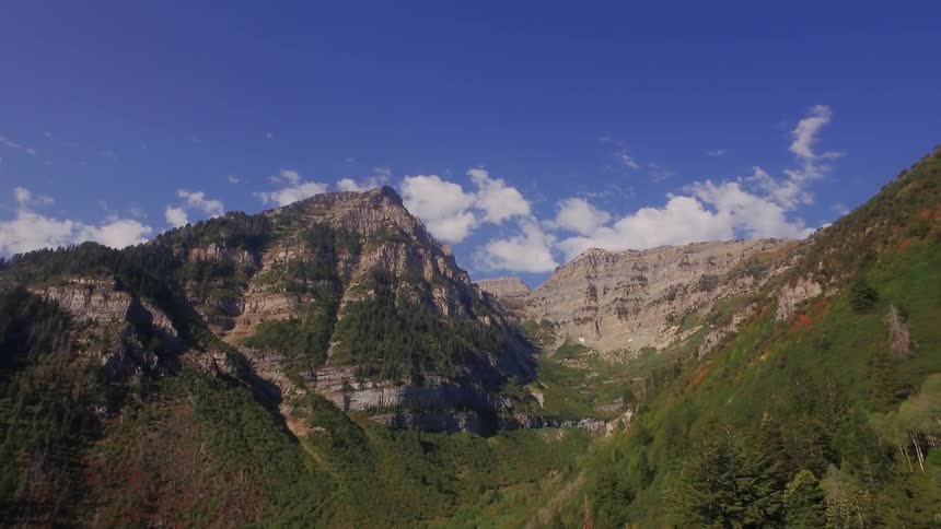 A lush green valley next to a mountain is being filmed by a drone