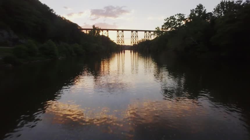 A river runs beneath an old railroad bridge at dusk