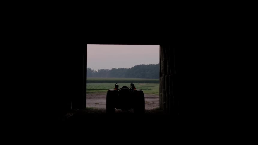 A red barn with a tractor inside opens up to a large crop