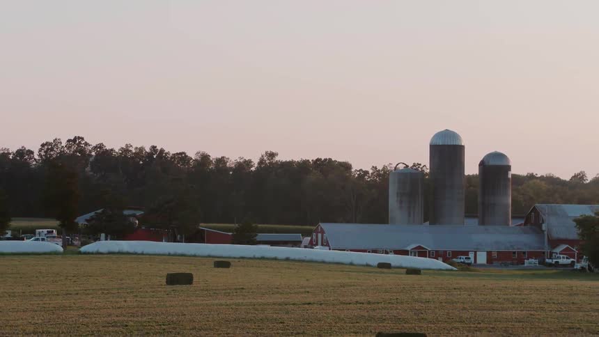 A large pasture with red barns is filmed