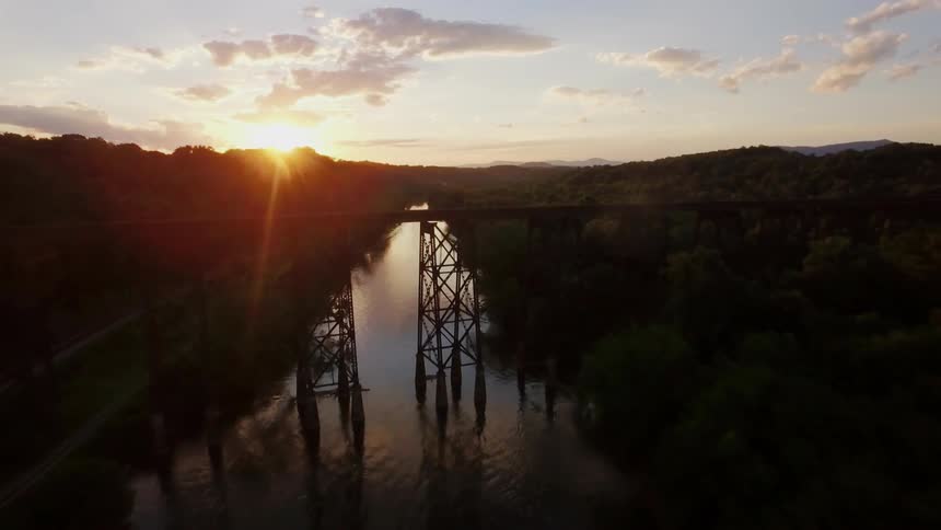 A bridge and small river are filmed by a drone at sunset