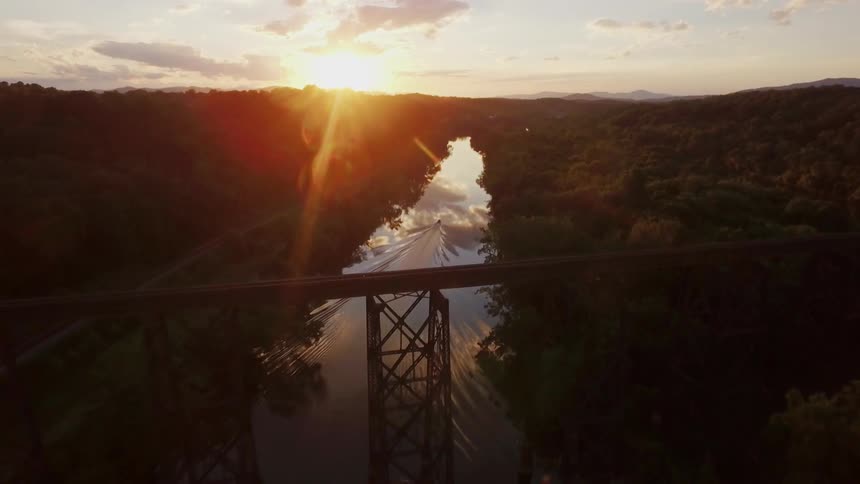 A boat travels past a railroad bridge on a river at dusk
