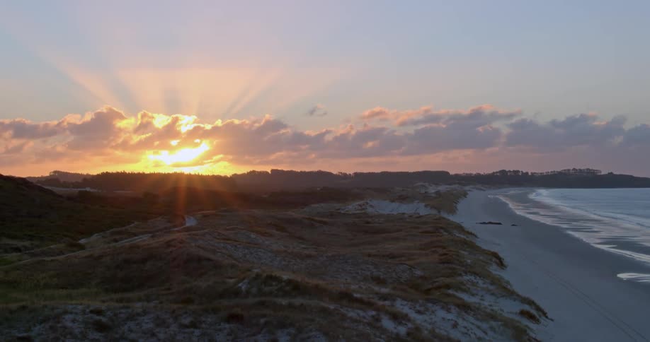 The sun is setting on the beach while waves crash ashore
