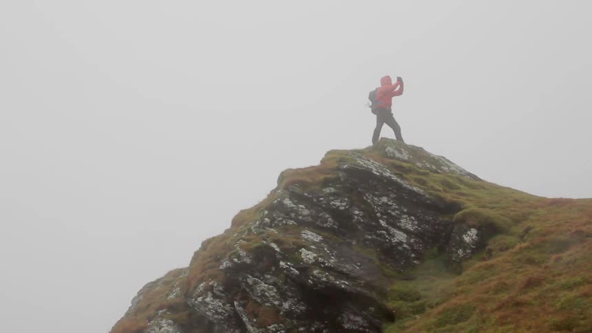 Person on top of a mountain peak takes photographs on a cloudy day