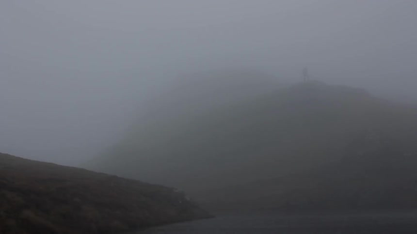 Hills covered in mist and a man standing atop a hill in the distance