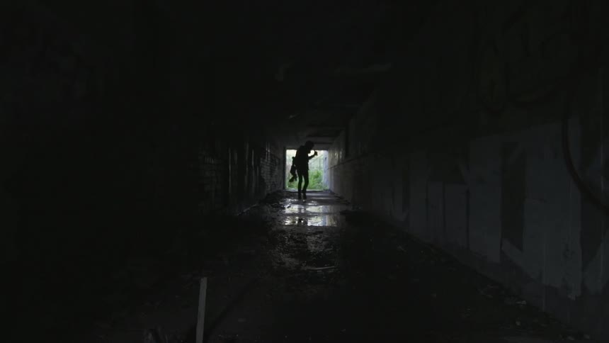 A silhouetted person walks down a dark tunnel