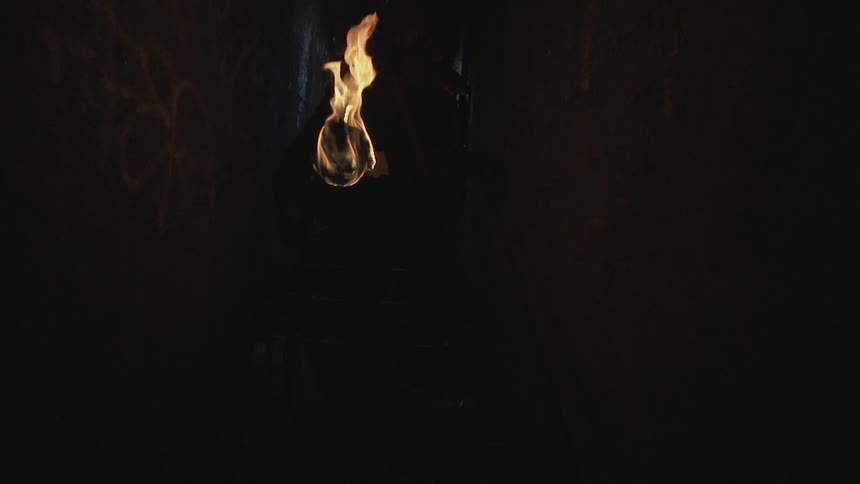 A person with a burning torch descending a dark stairwell