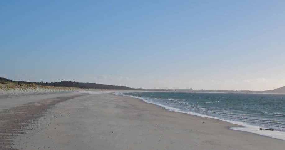 The waves slowly crash against the shore on a sunny day