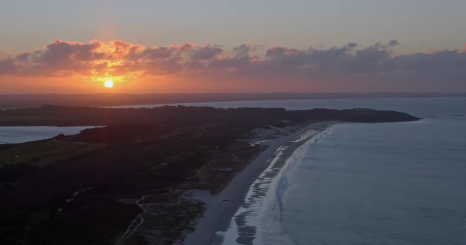 The sun is turning the sky crimson as it sets behind the island