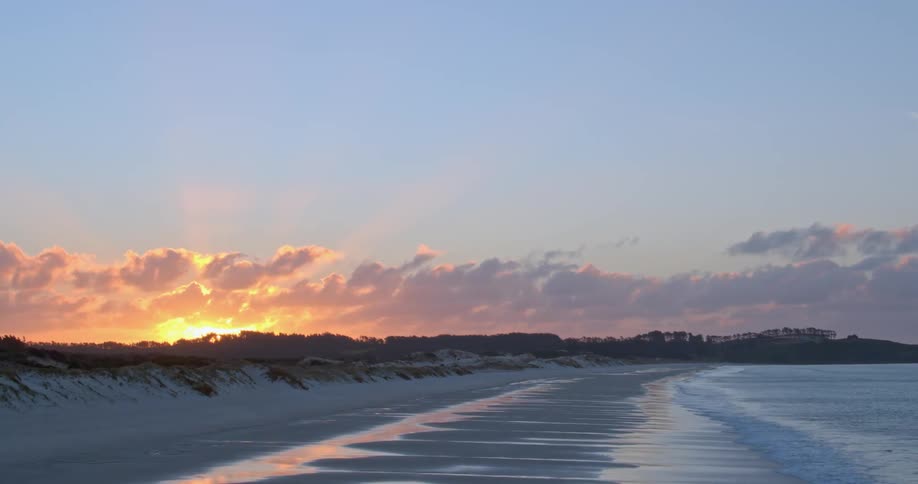 The sun is setting behind the trees by the beach