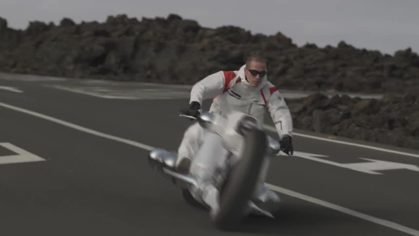 Someone is riding a futuristic looking motorcycle around a curve