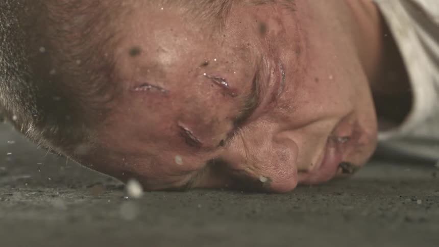 A man is being hit my dust and debris lays his head onto the concrete
