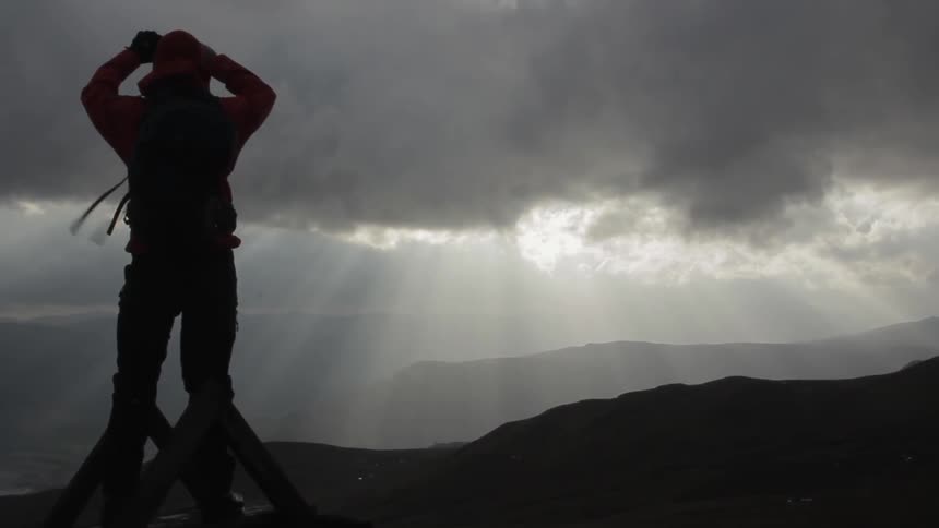Someone stands on a windy mountaintop taking a photograph on a cloudy day