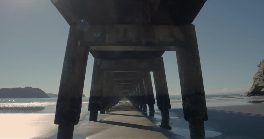 Someone is walking under a pier at the beach towards the ocean