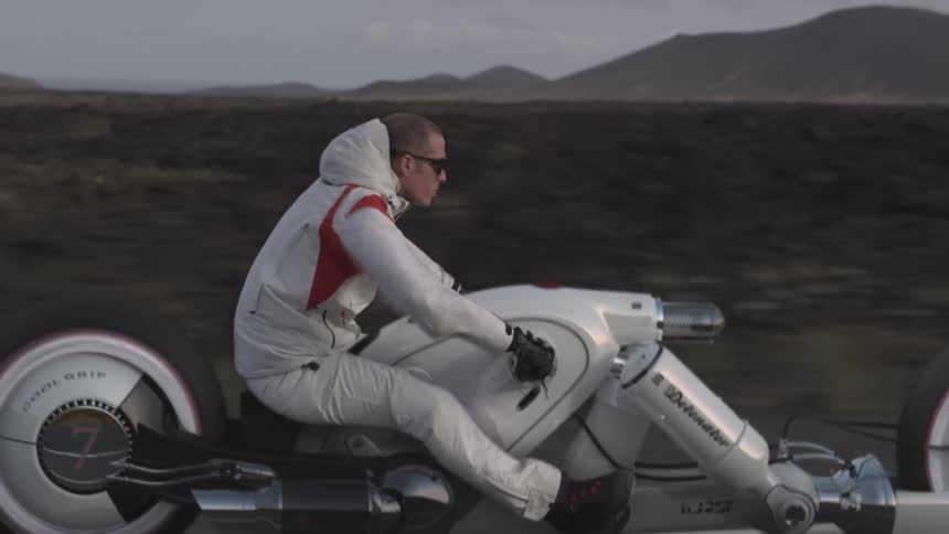 A man is riding a futuristic looking motorcycle in a desert landscape