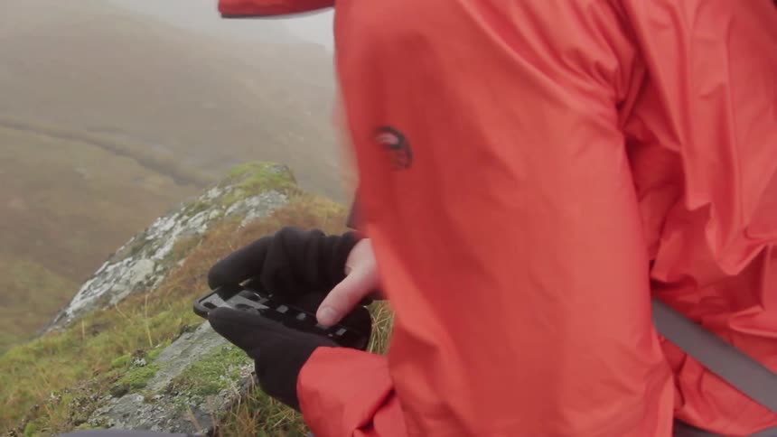 A person using a cell phone on top of a windy mountain