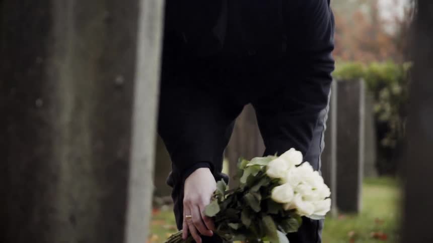 Man kneels in front of a headstone with roses