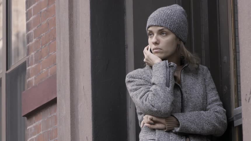 A woman is standing in a building doorway using her cellphone on a cold day