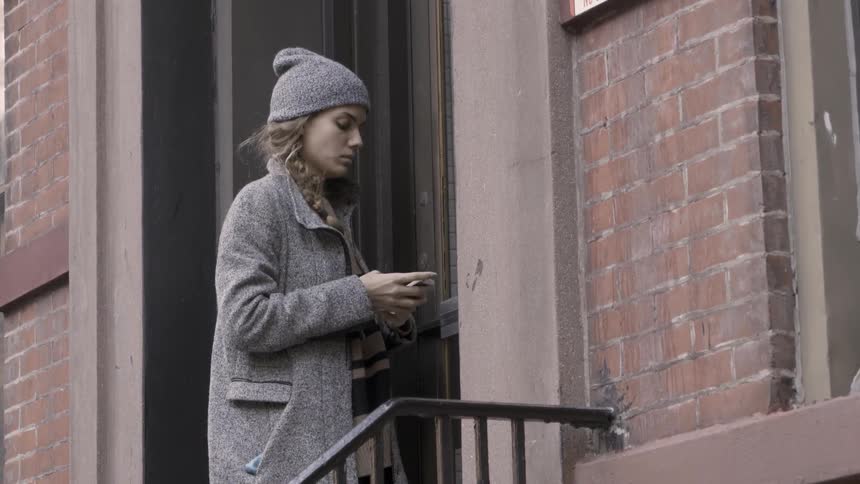 A woman stands by the door then uses her phone