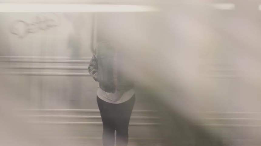 A woman stands on a platform as trains pass by