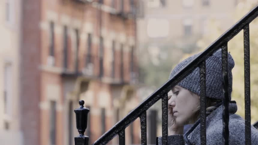 A woman sits on the steps of a building rubbing her face