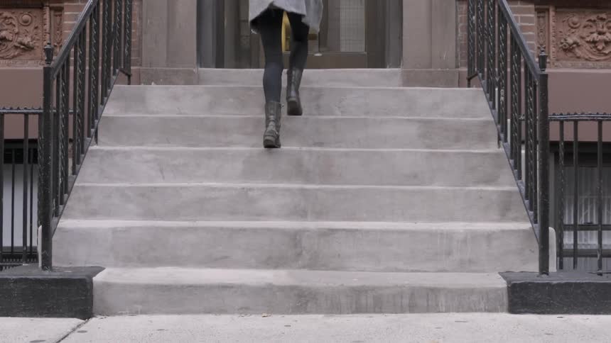 A woman is walking up the steps to a residential building on a cold day