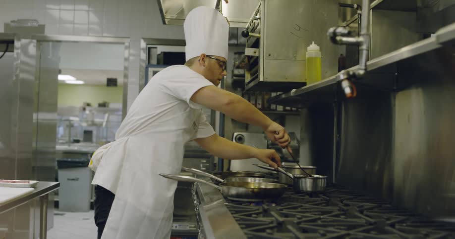 Man stirs several pots on a large stove