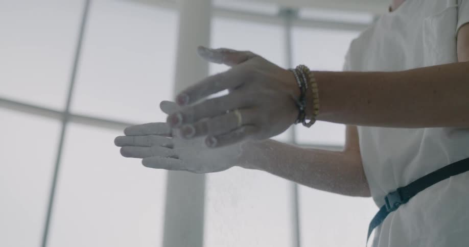 A person is dusting their hands with chalk at an indoor rock climbing gym
